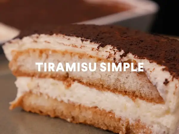Une part généreuse de tiramisu simple, parfait pour 10 personnes, avec ses couches de biscuits imbibés et de crème onctueuse, saupoudré de cacao.