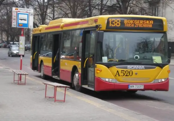 Żółto-czerwony autobus 138 warszawa z otwartymi drzwiami na przystanku.