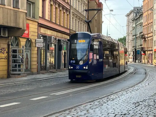 Niebieski tramwaj z napisem "Biskupin" na wyświetlaczu, jadący po brukowanej ulicy w mieście.