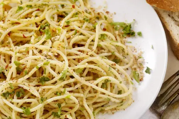Un piatto di spaghetti alla carrettiera, conditi con aglio, olio, peperoncino e prezzemolo fresco, accompagnati da pane rustico.