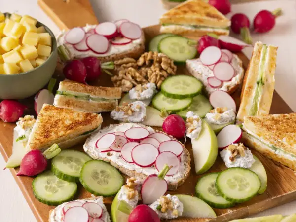 Un plateau d'apéro dinatoire plancha : toasts au fromage frais et radis, mini sandwichs concombre, dés de fromage, noix et quartiers de pomme.