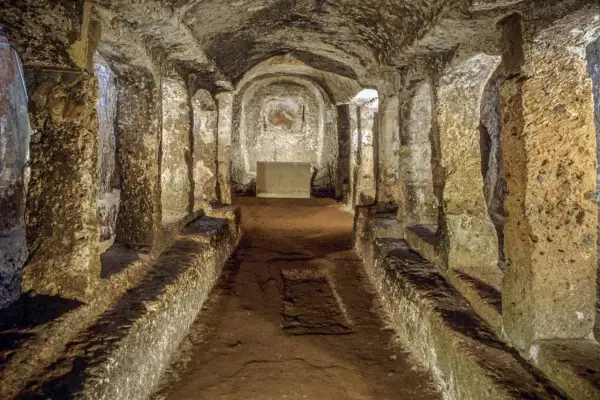 Corridoio sotterraneo con sedute in pietra e affreschi sbiaditi, parte dell'antico borgo di Sutri.