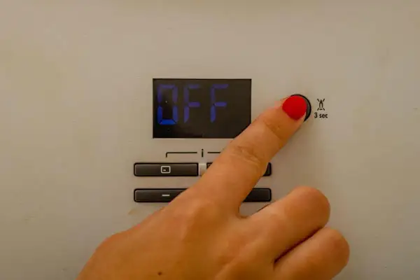 Dito che preme il pulsante per il reset caldaia Immergas. Lo schermo mostra "OFF".