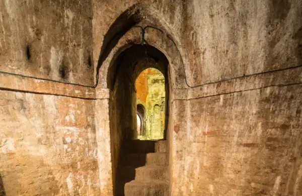 Un antico passaggio conduce ai **Bologna canali sotterranei**. Scale di pietra scendono nell'oscurità, tra muri di mattoni e archi in mattoni.