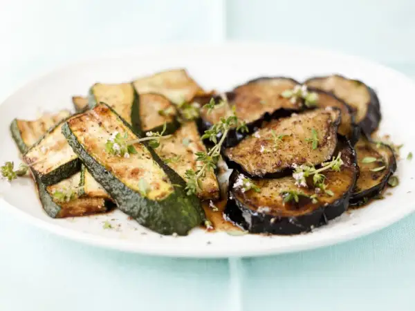 Gebratene zucchini und aubergine in der pfanne, garniert mit frischen Kräutern.