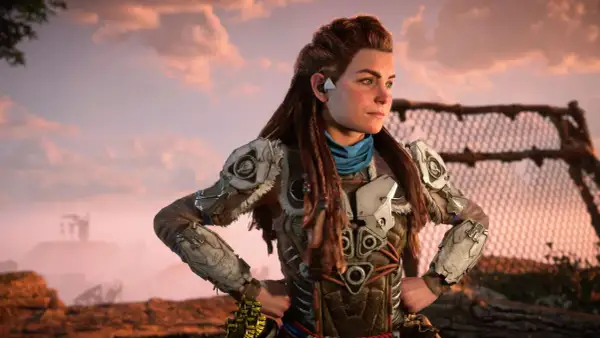 Aloy z Horizon Forbidden West, w zbroi z metalowymi płytami, patrzy w dal na tle zachodzącego słońca.