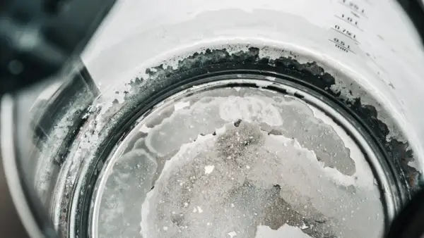 Gros plan sur le fond d'une bouilloire, montrant un tableau de dureté de l'eau avec des dépôts calcaires blancs et grisâtres.