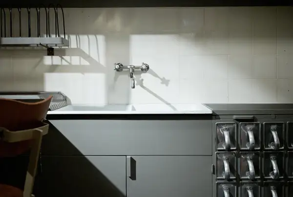 Stara kuchnia frankfurcka z ceramicznym zlewem, kranem i rzędem metalowych pojemników na przyprawy.