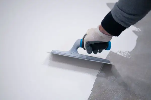 Mano con guanto stende resina, mostrando la differenza tra resina epossidica e poliuretanica per pavimenti.