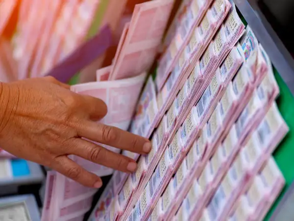 Dłoń wybiera losy loterii. To pokazuje, dlaczego zwycięzcy loterii kredytowych często wpadają w jeszcze większe długi, szukając kolejnej wygranej.