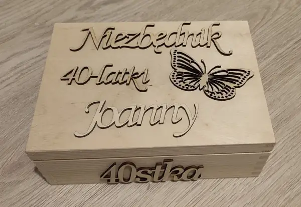 Drewniana skrzynka z napisem "Niezbędnik 40-latki Joanny" i motylem. Na froncie "40stka".