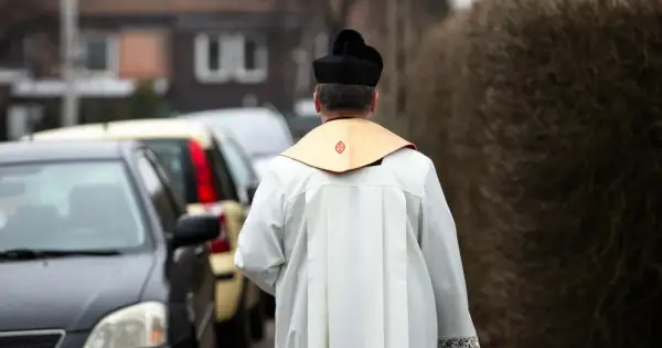Ksiądz w sutannie i birecie odchodzi od samochodów. Co się mówi do księdza na dowidzenia? "Szczęść Boże!