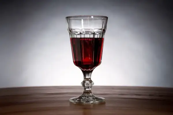 Szklanka z ciemnoczerwonym winem z jeżyn, stojąca na drewnianym blacie.