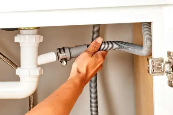 Hand connecting a dishwasher drain hose to a sink drain pipe.