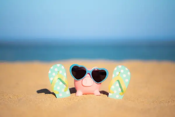Świnka skarbonka w okularach przeciwsłonecznych i klapki na plaży. To symbol oszczędzania na wakacje ZUS.