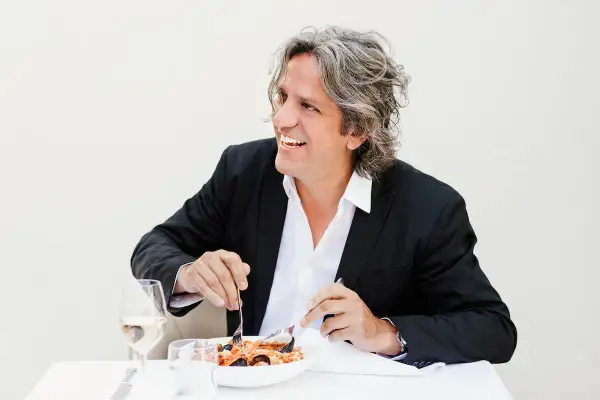 Giorgio Locatelli, chef stellato Michelin, sorride mentre gusta un piatto di pesce.