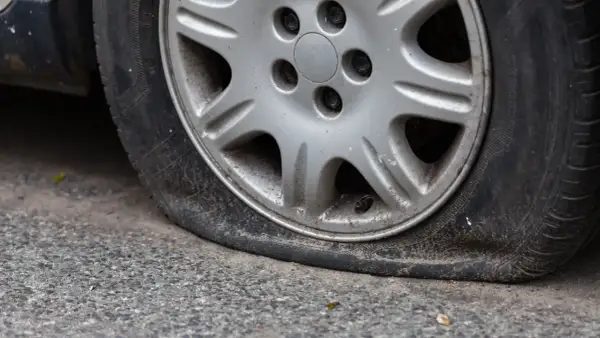 Gros plan sur une roue de voiture avec un pneu dégonflé, posée sur un trottoir gris. La jante est en alliage argenté.