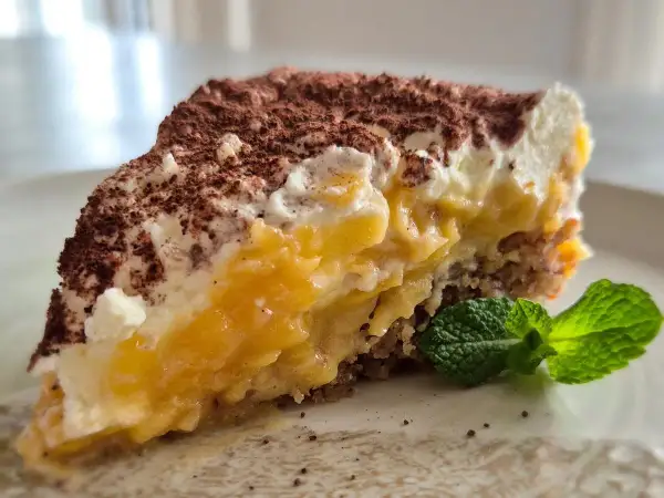 Ein saftiger Apfelkuchen-Schnitte mit cremiger Füllung, Kakao bestäubt und Minze garniert.