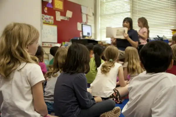 Kinderen zitten aandachtig te luisteren naar de juf die voorleest. Een mooi voorbeeld van leren van elkaar in de klas.