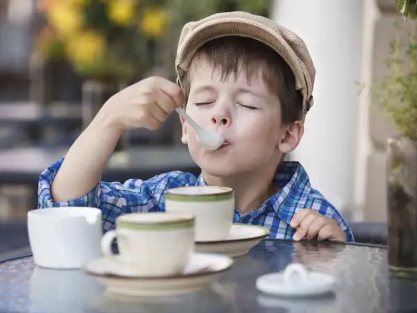 Bambino con cappellino gustando un delizioso cappuccino senza caffè, con gli occhi chiusi per il piacere.