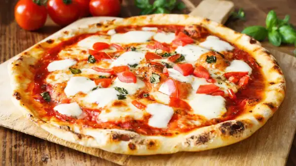 Pyszne ciasto na pizzę bez wyrastania, z pomidorami, mozzarellą i bazylią, na drewnianej desce.