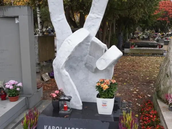 Monumentalna dłoń z symbolem pokoju na tle cmentarza. Wiele nagrobków tworzy ten zadumany zespół.