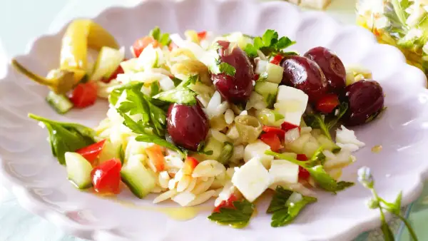 Ein erfrischender griechischer Orzo Salat mit Oliven, Feta, Gurken und Tomaten, garniert mit frischer Petersilie.