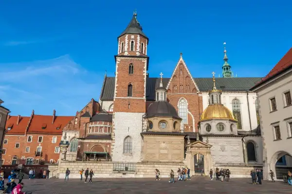 Majestatyczna katedra wawelska z cegły i kamienia, z dominującą wieżą i złotą kopułą, na tle błękitnego nieba.