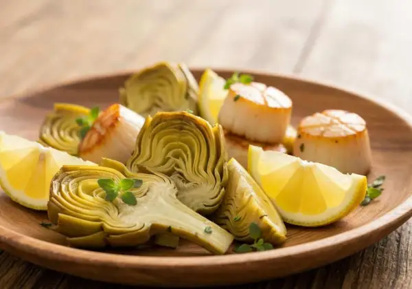Assiette de Saint-Jacques poêlées et fleur d'artichaut coupée, garnie de quartiers de citron et de quelques herbes fraîches.