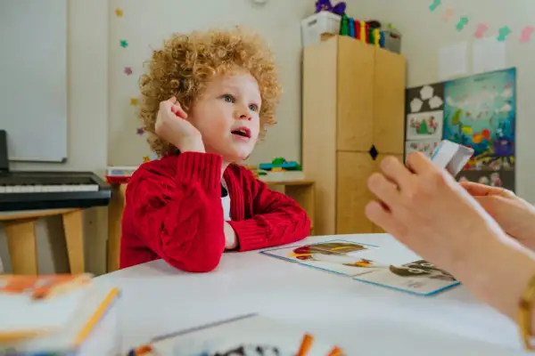 Chłopiec z kręconymi włosami, u którego zdiagnozowano orzeczenie Asperger, uczy się z kart obrazkowych.