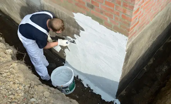 Mann dichtet mit Spachtel die Außenwand ab. Ein Eimer mit Abdichtmasse steht bereit.