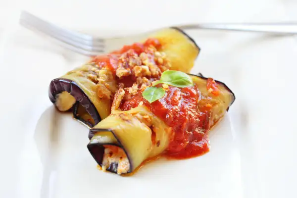Deliziosi involtini di melanzane alla siciliana, ripieni e conditi con sugo rosso e basilico fresco, pronti per essere gustati.