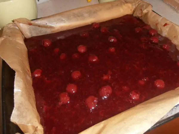 Gotowe do pieczenia ciasto bajka z wiśniami w blaszce wyłożonej papierem. Słodka, czerwona masa z całymi owocami.