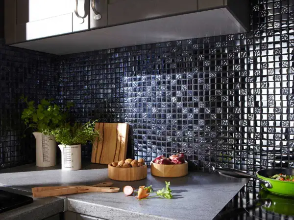 Crédence noire brillante, idéale pour une cuisine moderne. Des herbes fraîches, des oignons et des noix sur le plan de travail. Quelle crédence choisir pour un style audacieux ?