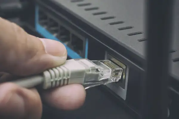 Dłoń podłącza kabel sieciowy kategorii do routera, zapewniając stabilne połączenie internetowe.