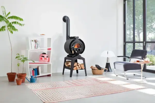Ein gemütliches Wohnzimmer mit einem Bullerjan B3 Keramik Ofen, der Holzscheite wärmt. Daneben ein Bücherregal mit einer bunten Maske.