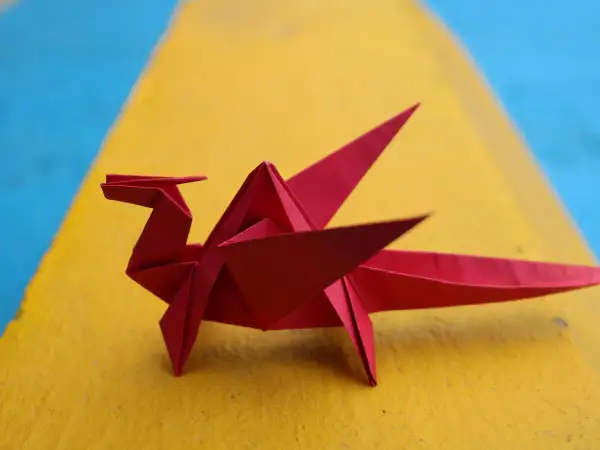 Un dragón rojo de papiroflexia fácil descansa sobre una superficie amarilla y azul.
