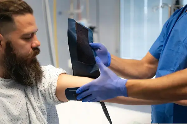 Medyk w niebieskich rękawiczkach zakłada mankiet na ramię pacjenta. Badanie może pomóc ocenić poziom lipoproteiny, co to jest i jak wpływa na zdrowie.