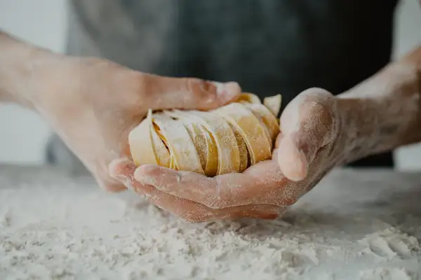 Dłonie trzymające świeży, pokrojony makaron tagliatelle, oprószony mąką.