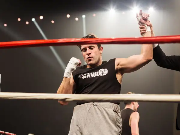 A boxer's arm is raised in victory, a moment of triumph in amateur vs professional boxing. The crowd roars as the referee declares the winner.