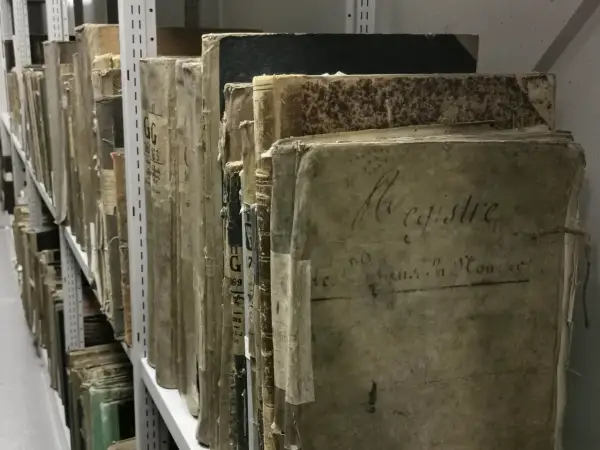 Des registres anciens, certains marqués "archive 07", s'alignent sur des étagères métalliques, témoins silencieux du temps.