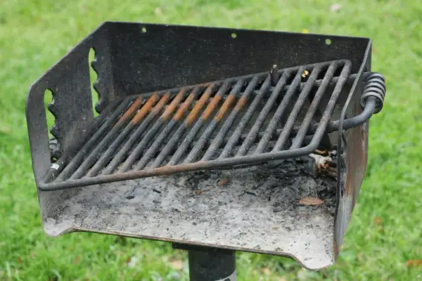 Ett rostigt grillgaller med aska under, redo för nästa grillkväll i parken.