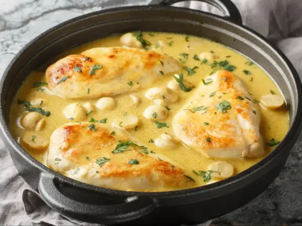 Aromatyczna potrawka z kurczaka w kremowym sosie z pieczarkami, posypana świeżą natką pietruszki, podana w czarnym naczyniu.