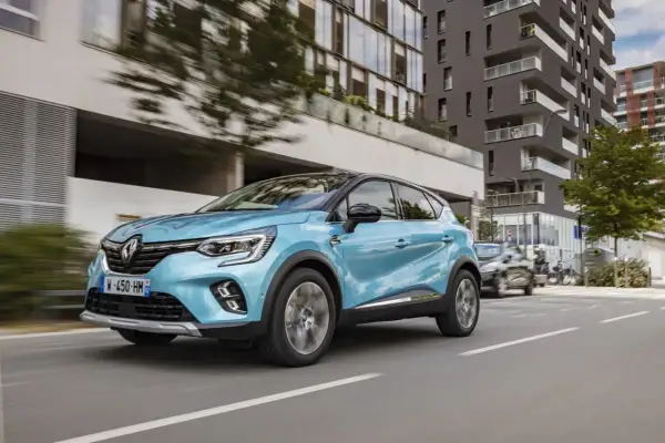 Un coche azul phev Renault Captur circula por una calle urbana moderna, con edificios de cristal y hormigón al fondo.