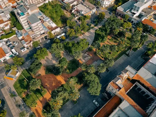 Un parco urbano rigenerato, con palme e alberi, circondato da edifici residenziali e commerciali.