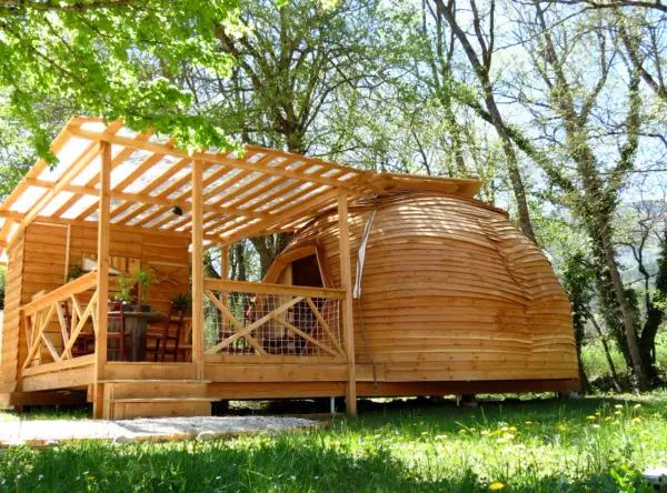 Cabane en bois et dôme de glamping Paca, avec terrasse et table extérieure, dans un cadre verdoyant.