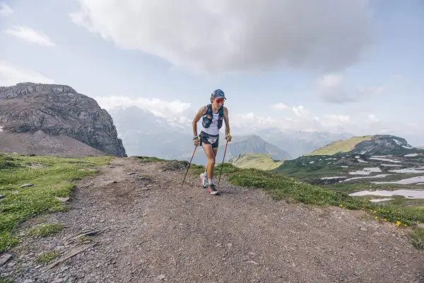 Corredor/a de montaña en un sendero rocoso, con bastones y vistas alpinas. Esto es trail running, pura aventura.