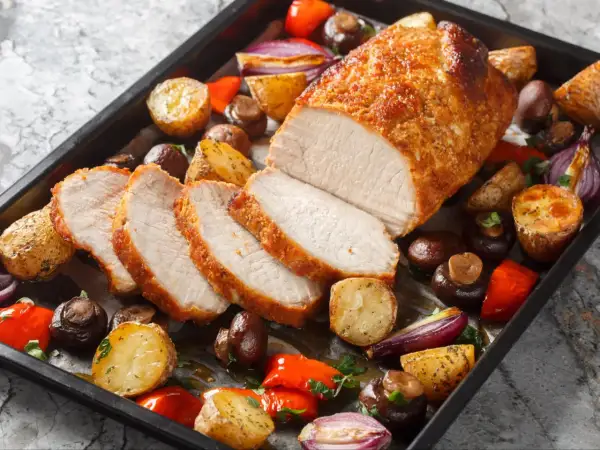 Schab pieczony w piekarniku, soczysty i rumiany, podany z pieczonymi ziemniakami, pieczarkami, papryką i czerwoną cebulą.