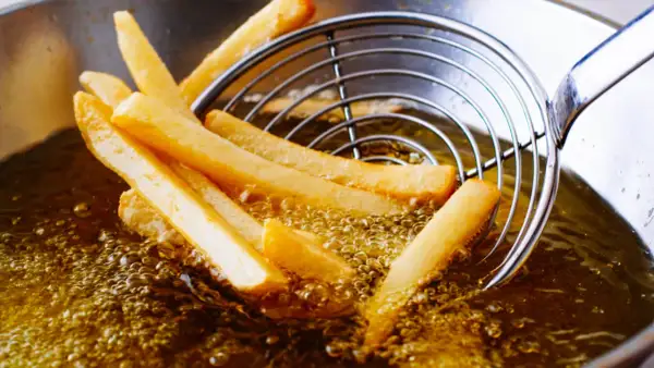 Patatine fritte dorate che sfrigolano nell'olio di oliva, pronte per essere gustate.
