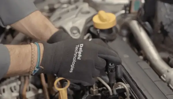 Manos con guantes negros trabajando en un motor diésel, manipulando un inyector.